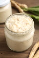 Tasty horseradish sauce and roots on wooden table, closeup