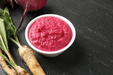 Tasty horseradish sauce with beetroot, roots and vegetable on black table, closeup. Space for text