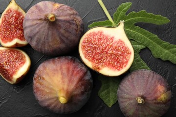 Fresh ripe figs and green leaf on black textured table, flat lay