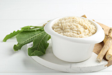 Tasty horseradish sauce and roots on white wooden table, closeup