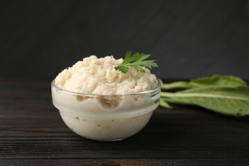 Tasty horseradish sauce with parsley and roots on black wooden table, closeup