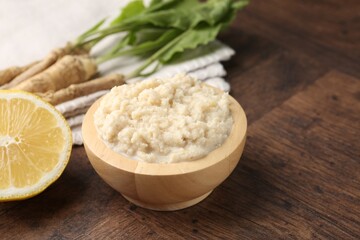 Tasty horseradish sauce and roots on wooden table, closeup