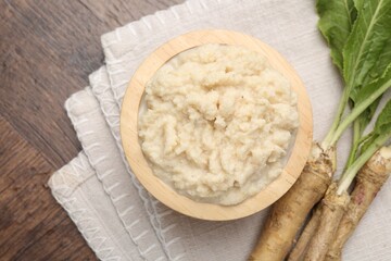 Tasty horseradish sauce and roots on wooden table, flat lay