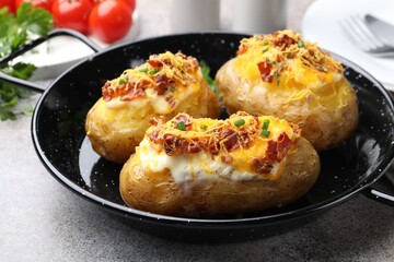 Tasty stuffed baked potatoes in baking dish on grey table, closeup
