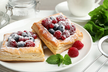 Tasty puff pastries with berries, powdered sugar and mint on white wooden table, closeup