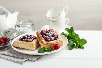 Tasty puff pastries with berries, powdered sugar and mint on white wooden table