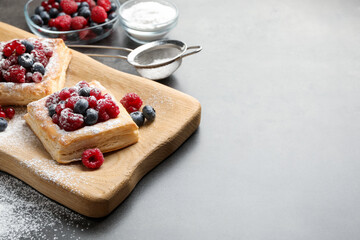 Tasty puff pastries with berries and powdered sugar on grey table, closeup. Space for text