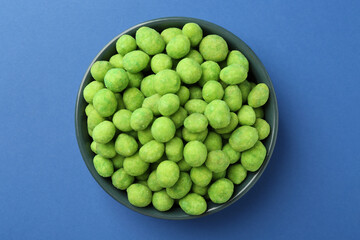 Delicious wasabi coated peanuts in bowl on blue background, top view