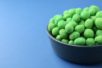 Delicious wasabi coated peanuts in bowl on blue background, closeup. Space for text