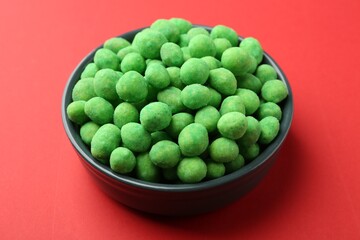 Delicious wasabi coated peanuts in bowl on red background, closeup