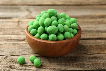 Delicious wasabi coated peanuts in bowl on wooden table, closeup
