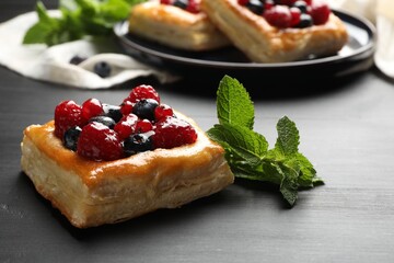 Tasty puff pastries with berries and mint on grey wooden table, closeup