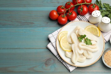 Raw squid rings, parsley, lemon, spices and tomatoes on light blue wooden table, flat lay. Space for text