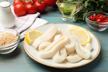 Raw squid rings, lemon and spices on light blue wooden table, closeup