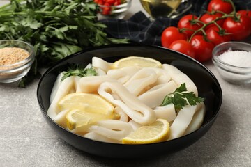 Raw squid rings, lemon, parsley, spices and products on grey textured table, closeup