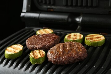 Electric grill with beef and zucchini on black table, closeup