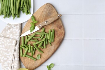 Cut green bean pods and knife on white tiled table, top view. Space for text
