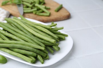 Cut green bean pods on white tiled table, closeup. Space for text