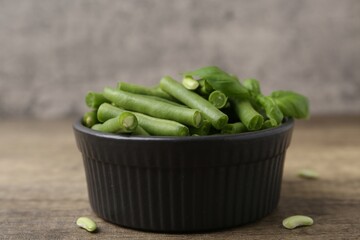 Pieces of fresh green beans in bowl on wooden table, closeup