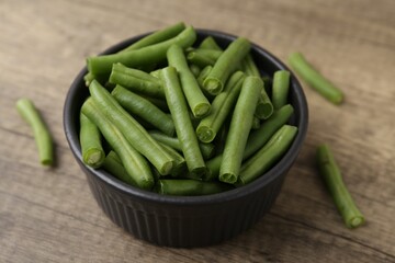 Pieces of fresh green beans in bowl on wooden table, closeup