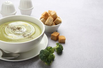Tasty broccoli cream soup served with croutons on light grey table, closeup. Space for text