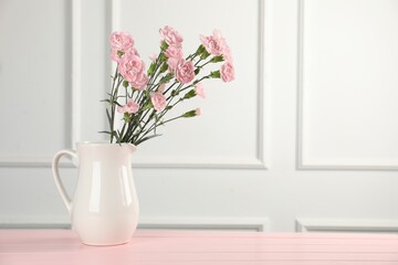 Beautiful carnation flowers in vase on pink wooden table near white wall indoors, space for text