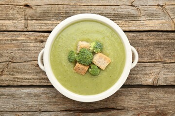 Tasty broccoli cream soup with croutons in bowl on wooden table, top view