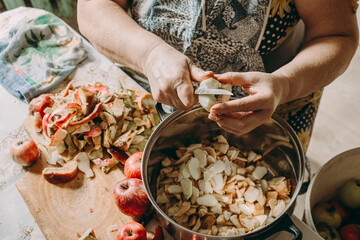 Old woman cuts apples for jam. Red ripe apples on the table next to the jam pot. An elderly woman makes jam in her cottage on a farm. Conservation and harvesting. Homemade delicious food