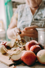 Old woman cuts apples for jam. Red ripe apples on the table next to the jam pot. An elderly woman makes jam in her cottage on a farm. Conservation and harvesting. Homemade delicious food