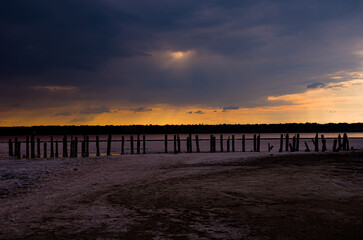 Obraz premium Dramatic Sunset Over Salt Lake with Ancient Wooden Pillars
