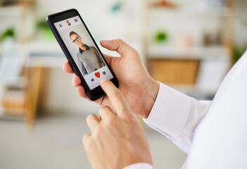 Closeup of a person using a smartphone dating app, tapping the heart icon to like a user's profile in a living room, showing screen and finger interaction. Find love and online dating concept.
