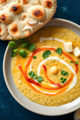 a close-up, top-down view of a bowl of golden-orange curry with chicken pieces and a vibrant red swirl, garnished with fresh cilantro, and accompanied by soft naan bread.