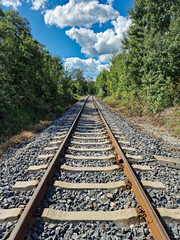 Railway track with concrete sleepers, perspective lines converging in the distance, sunny day with clouds, symbolizing journey, future, adventure, and travel concept.