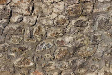 Old stone wall with irregular natural rocks set in mortar. Weathered textures, earthy tones, rough patterns, ideal for background, design element in architectural, historical, rustic-themed designs