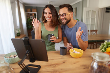 A couple sits at a kitchen table, sharing breakfast and smiling as they connect with someone online. The atmosphere is warm and inviting, filled with morning light.