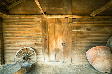 Interior of a traditional Georgian wooden house with old wooden door, cart wheel and wine vessel. Rustic textures and historic charm