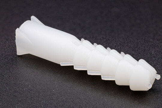Side-angle view of a white plastic wall anchor on a dark, textured background