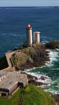 Petit Minou Lighthouse on rocky islet, stone tower, causeway, and blue sea with waves, Plouzan&eacute;, Brittany, France. Aerial forward, vertical format