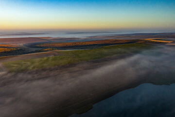 Aerial view of misty farmland landscape with fields and water at sunrise
