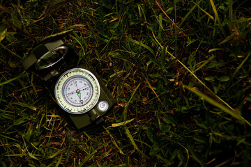 Green metal compass lying on the grass, concept of tourist equipment, finding the right direction of the path. © Mariya