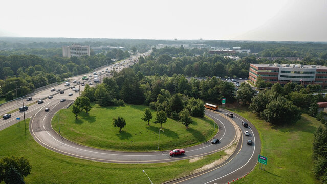 Aerial view of a looping highway interchange surrounded by verdant trees and buildings under a hazy sky, Philadelphia, Pennsylvania, United States.