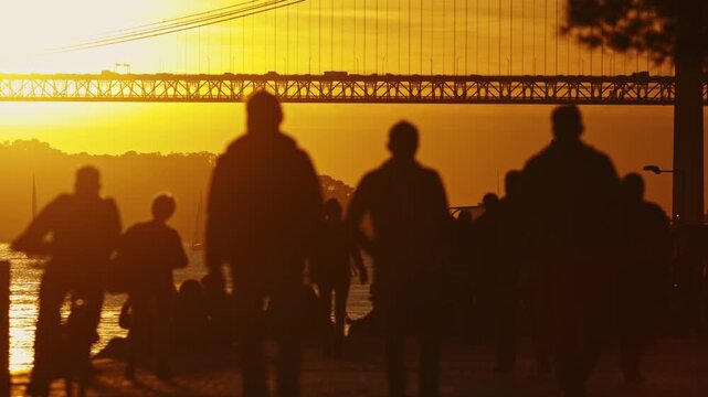 Crowd of silhouettes walking at sunset near lisbon bridge