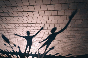 The image captures the shadows of two distinct figures, which are dynamically casting expressive arm gestures onto a paved surface