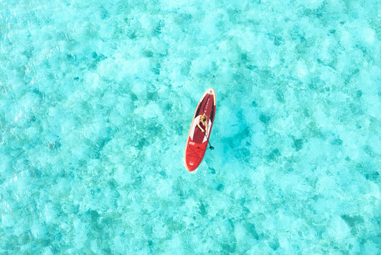 Aerial view of a single paddleboard glides across the turquoise expanse, a vibrant streak against the clear waters, Thoddoo, Alif Alif Atoll, Maldives.