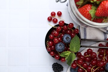 Ripe red currants, blueberries and mint leaves on white tiled table, flat lay. Space for text