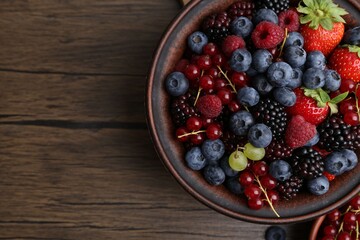 Different ripe berries in bowls on wooden table, flat lay. Space for text