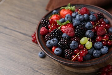 Different ripe berries in bowl on wooden table, closeup. Space for text