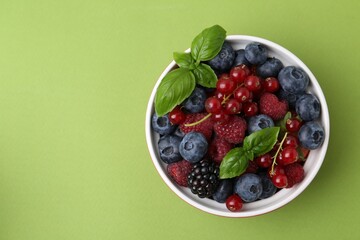 Different ripe berries and basil leaves on green background, top view. Space for text