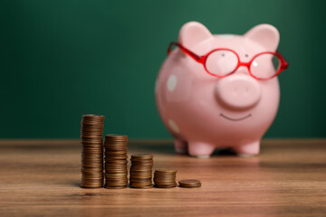 Coins and piggy bank on wooden table against green background, selective focus