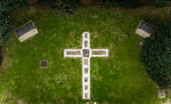 Aerial view of a stone cross design on a lush green lawn, flanked by simple benches, creating a serene and contemplative space, The Hill, New South Wales, Australia.
